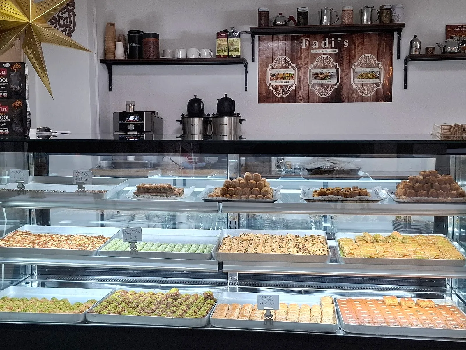Gläserne Theke voller Baklava und orientalischem Gebäck, darüber das Schild Fadi's – Les Délices d’Orient und ein goldener Stern